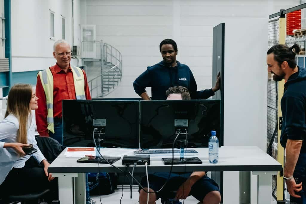 Fem personer arbejder sammen foran et computersystem for at lære, hvordan man betjener Autostore-systemet. 