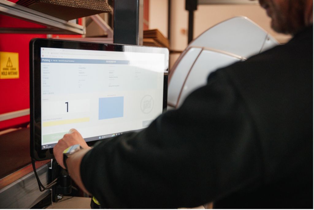 En mand bruger en touchskærm til at færdiggøre ordrer i et AutoStore-system.